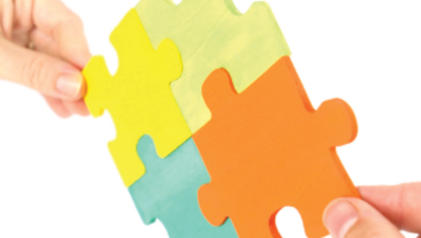 Zwei Hände setzen grosse farbige Puzzleteile zusammen